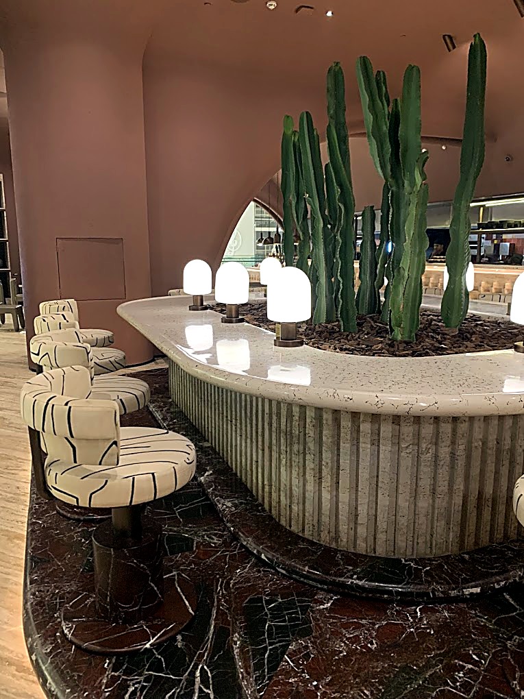 Marble island bar with a planted cactus centrepiece and cream tub chairs under warm lighting