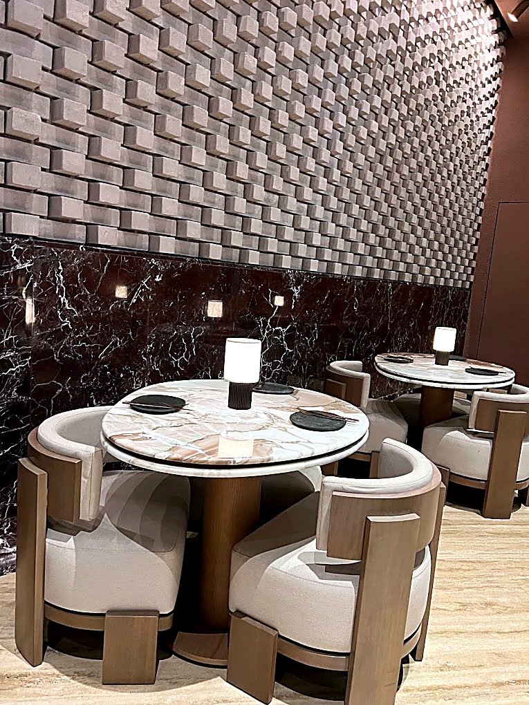 Dining area with a woven textured feature wall, marble tables and cream tub chairs