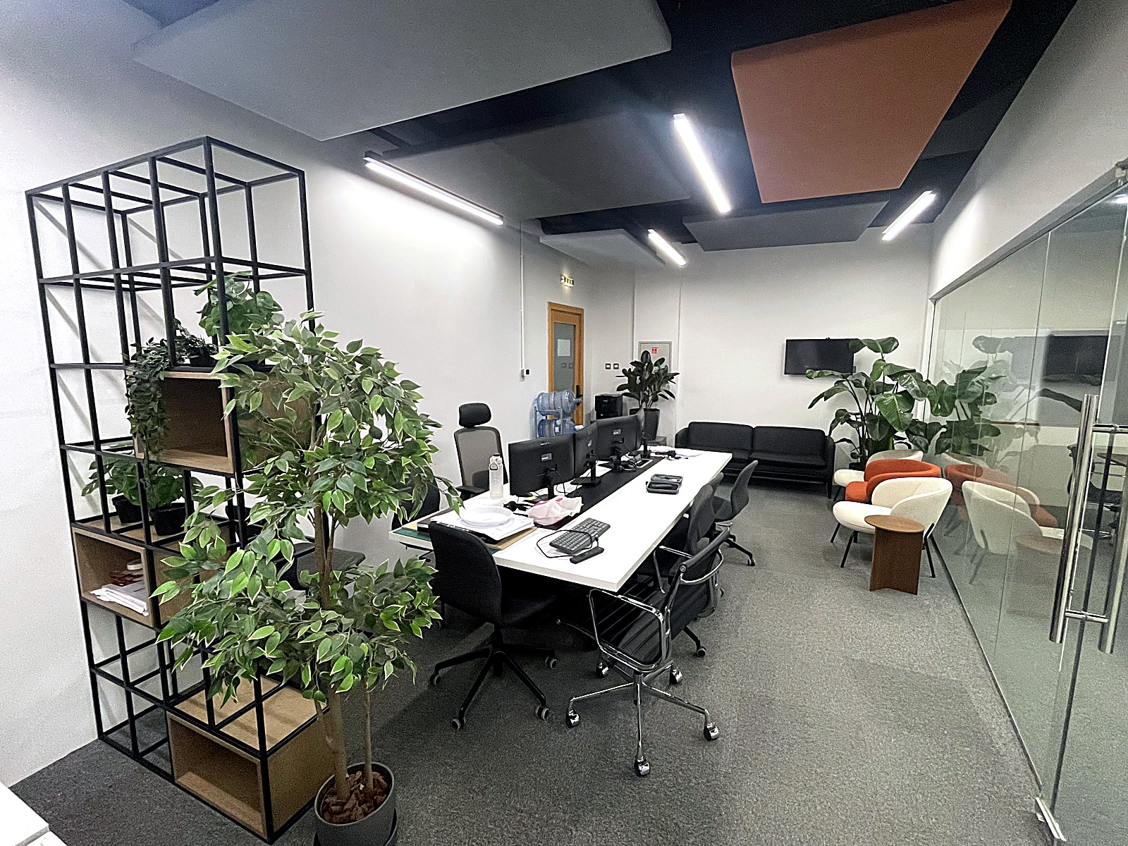 Open office with angular navy and rust acoustic ceiling baffles, a black steel shelving frame and planting