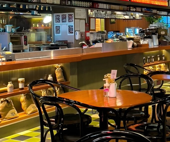 Cafe seating with bentwood chairs beside a timber counter and menu board shelving