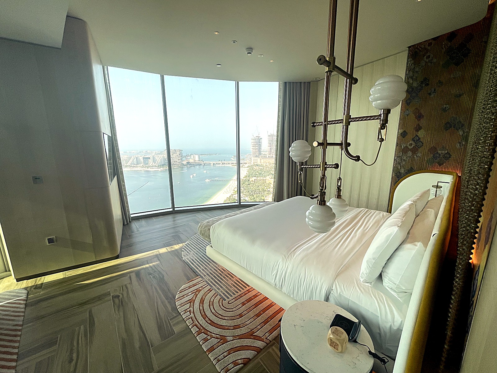 Bedroom with an upholstered bed and curved sofa beside floor to ceiling sea view windows