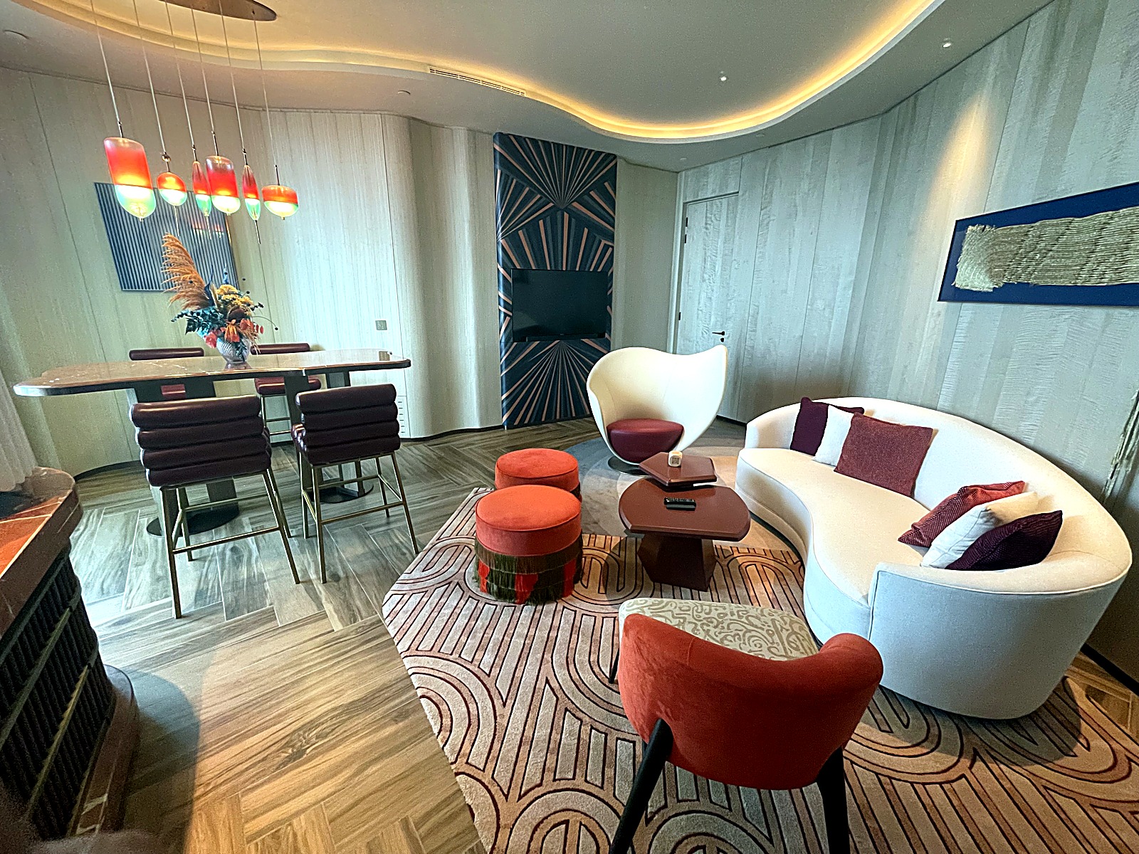 Suite lounge with a curved white sofa, rust accent chairs and a dining table on a patterned carpet